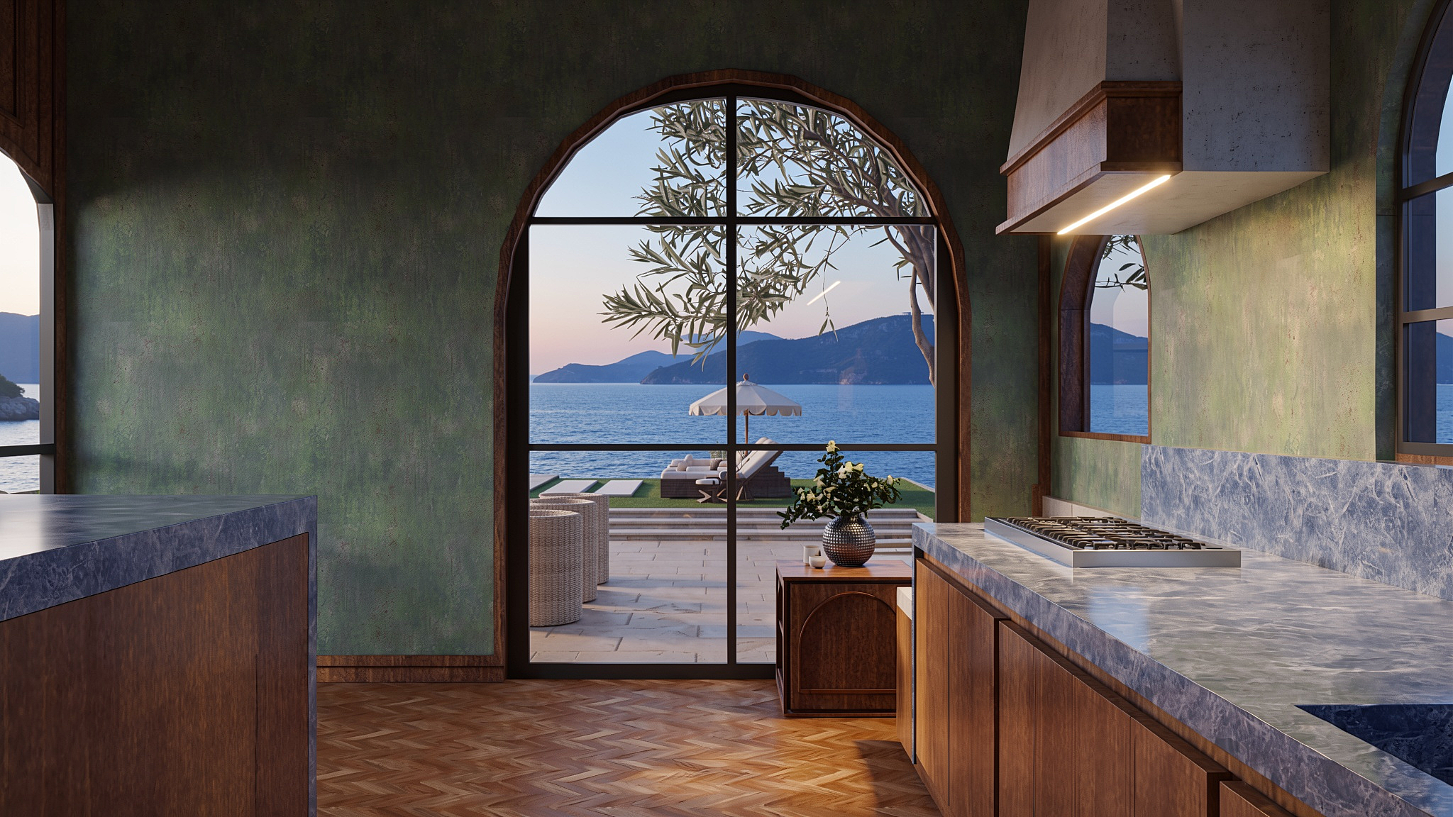 Kitchen with an arched steel window opening to an olive tree and oceanfront terrace at dusk